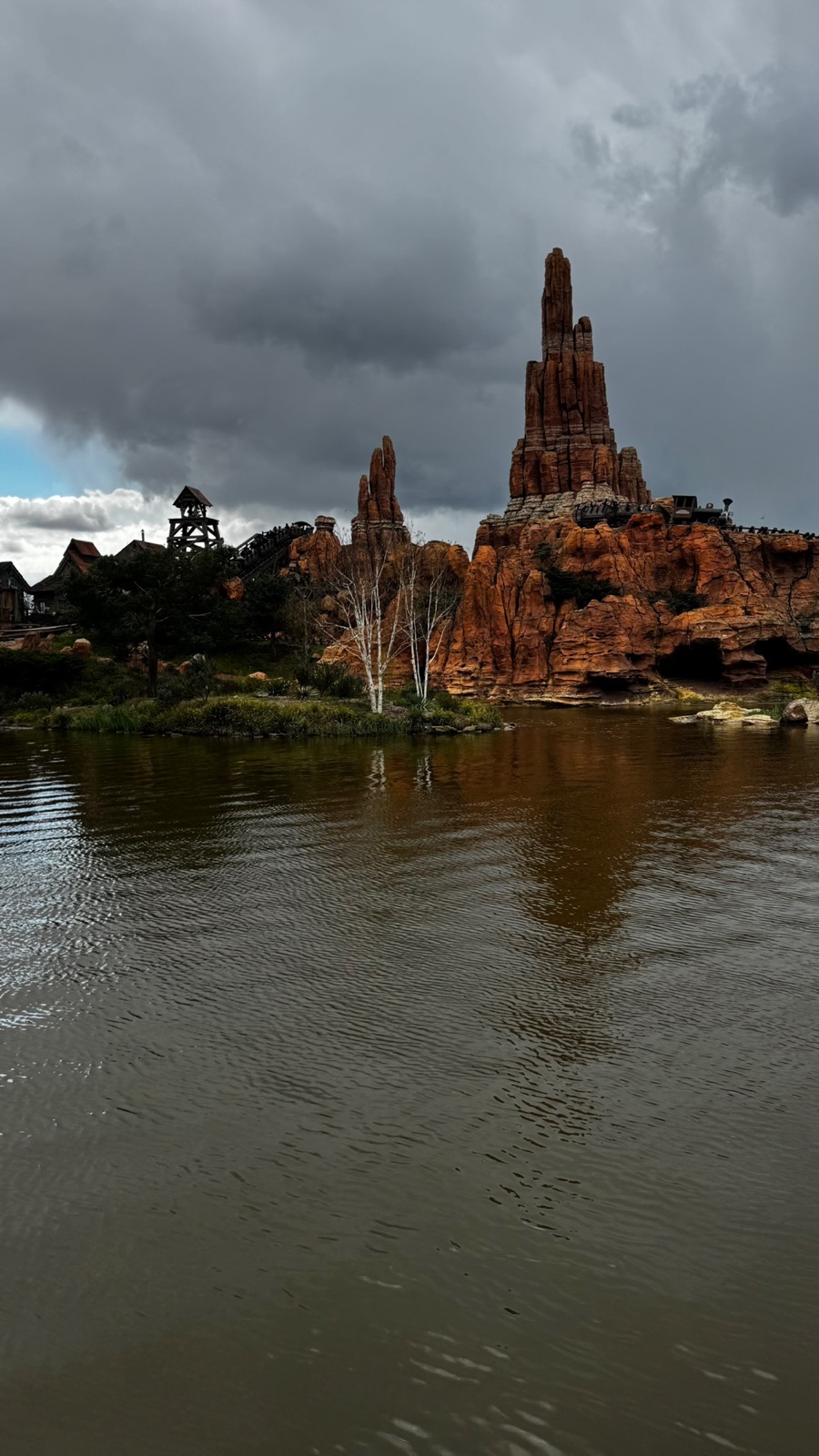 Οι κόκκινες βραχώδεις αιχμές του Big Thunder Mountain με ένα τρενάκι ορυχείου να διασχίζει την κορυφογραμμή, με σκούρα σύννεφα καταιγίδας από πάνω