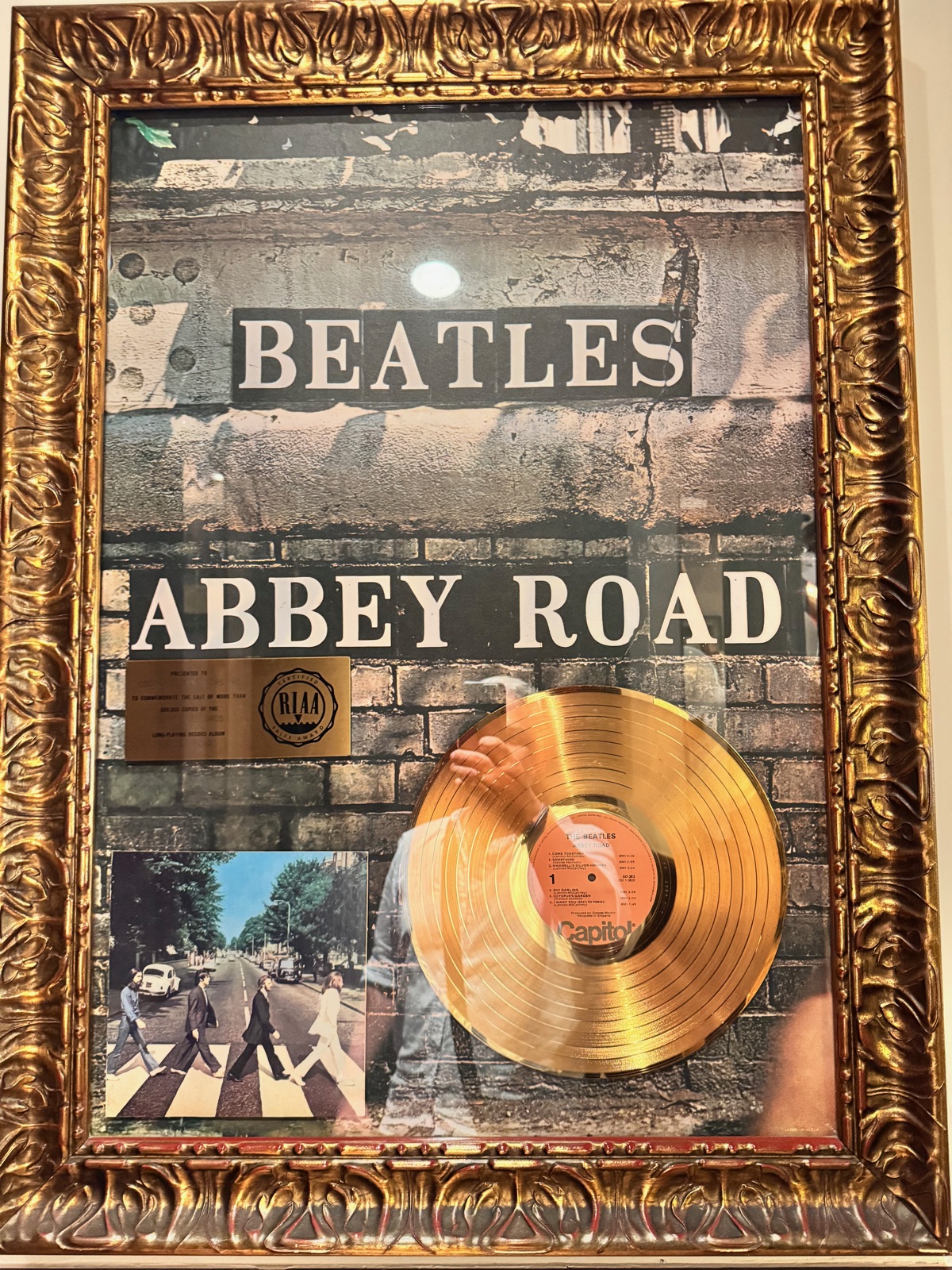 Ένας χρυσός δίσκος για το άλμπουμ Abbey Road των Beatles σε μια περίτεχνη χρυσή κορνίζα στον τοίχο, με μια μικρή εκτύπωση της φωτογραφίας της διάβασης δίπλα