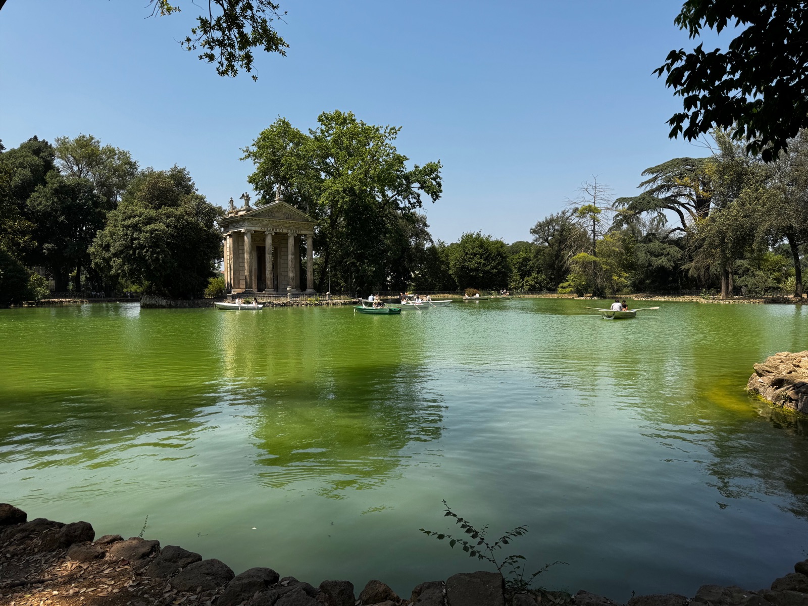 Η φαρδιά πράσινη λίμνη στη Βίλα Μποργκέζε με βάρκες κωπηλασίας στο νερό και τον μικρό ναό ανάμεσα σε δέντρα στην απέναντι πλευρά