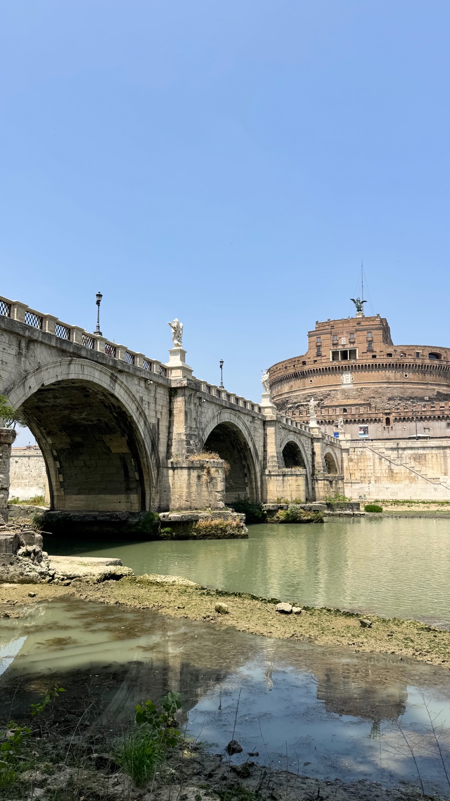 Οι καμάρες της Ponte Sant Angelo πάνω από τον χαμηλό πράσινο Τίβερη με τον κύλινδρο του Castel Sant Angelo να υψώνεται πίσω
