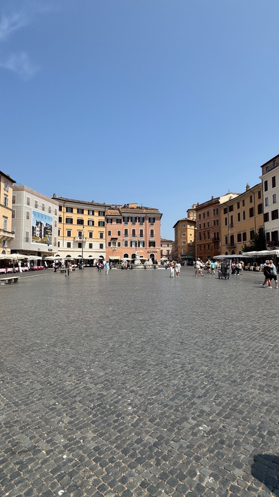 Το μακρύ οβάλ της Piazza Navona με ένα σχεδόν άδειο πεζοδρόμιο, τέντες και κτίρια να πλαισιώνουν το βάθος