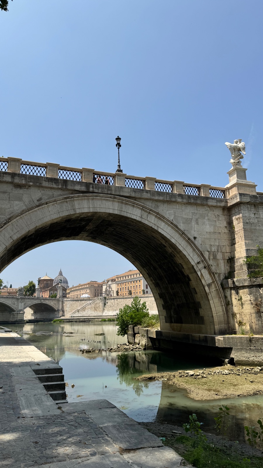 Μια καμάρα της Ponte Sant Angelo να πλαισιώνει τον μακρινό θόλο του Αγίου Πέτρου πέρα από το ποτάμι, αγάλματα στο στηθαίο από πάνω